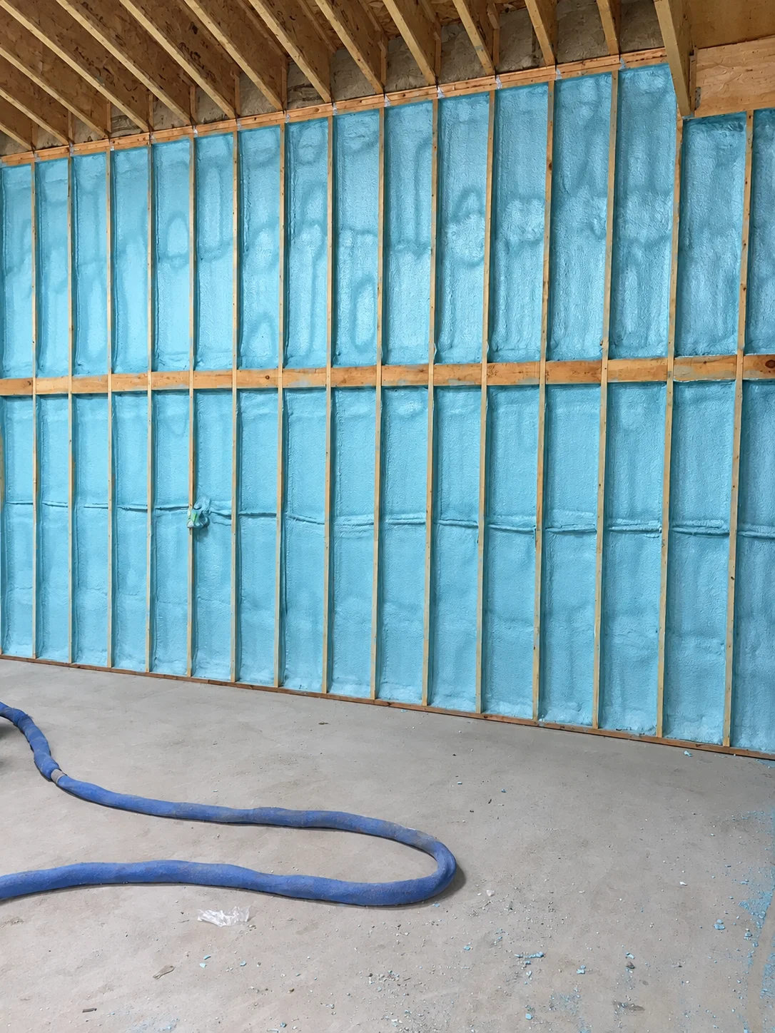 Citadel project: blue insulated wall with exposed framing and a hose on the floor